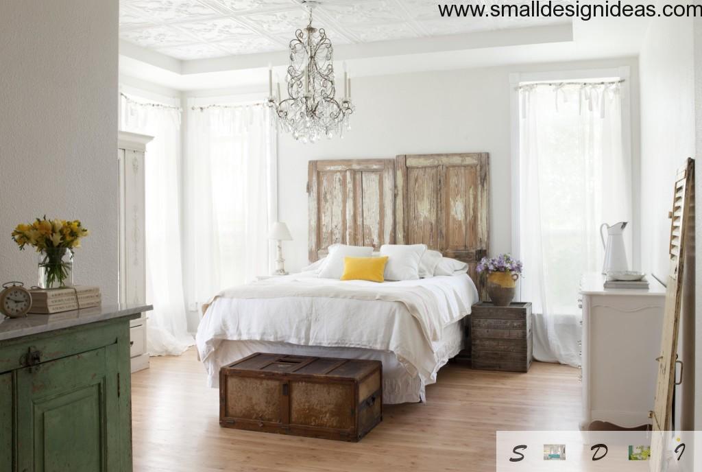 Vintage white bedroom interior with unusual wooden bedhead and outlandish chandelier