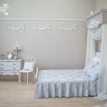 Light painted bedroom with fretwork and shawl at the bedhead and modest vintage furniture at the bedside