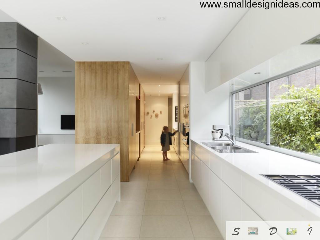 Long galley kitchen in the country house leading to the long hall. White scheme decoration