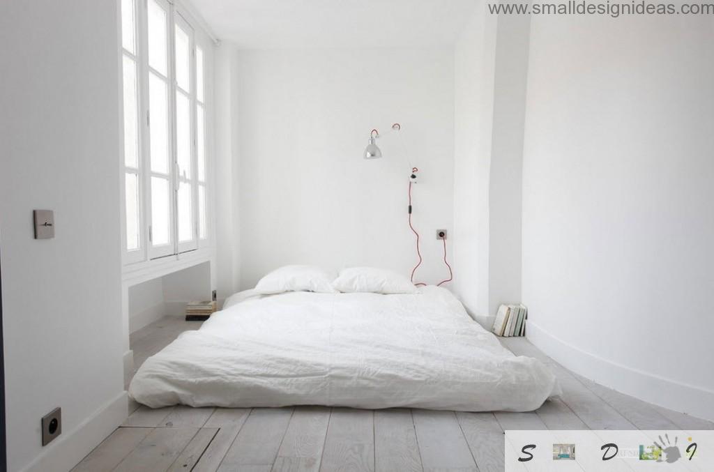 Absolutely white bedroom with mattress on the wooden floor and accent red wired lamp