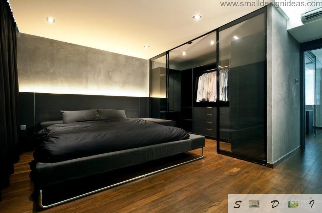 Chic black bed in the dark interior of the men`s bedroom with wardrobe full of fashionable clothes