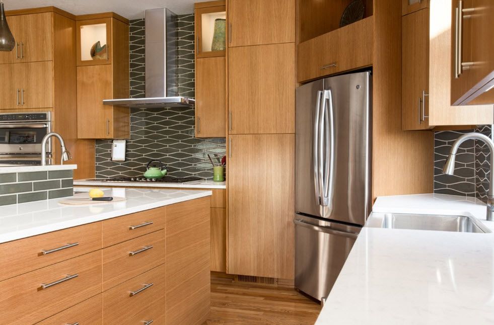 Light wooden trimmed kitchen furniture with steel splashback and fridge