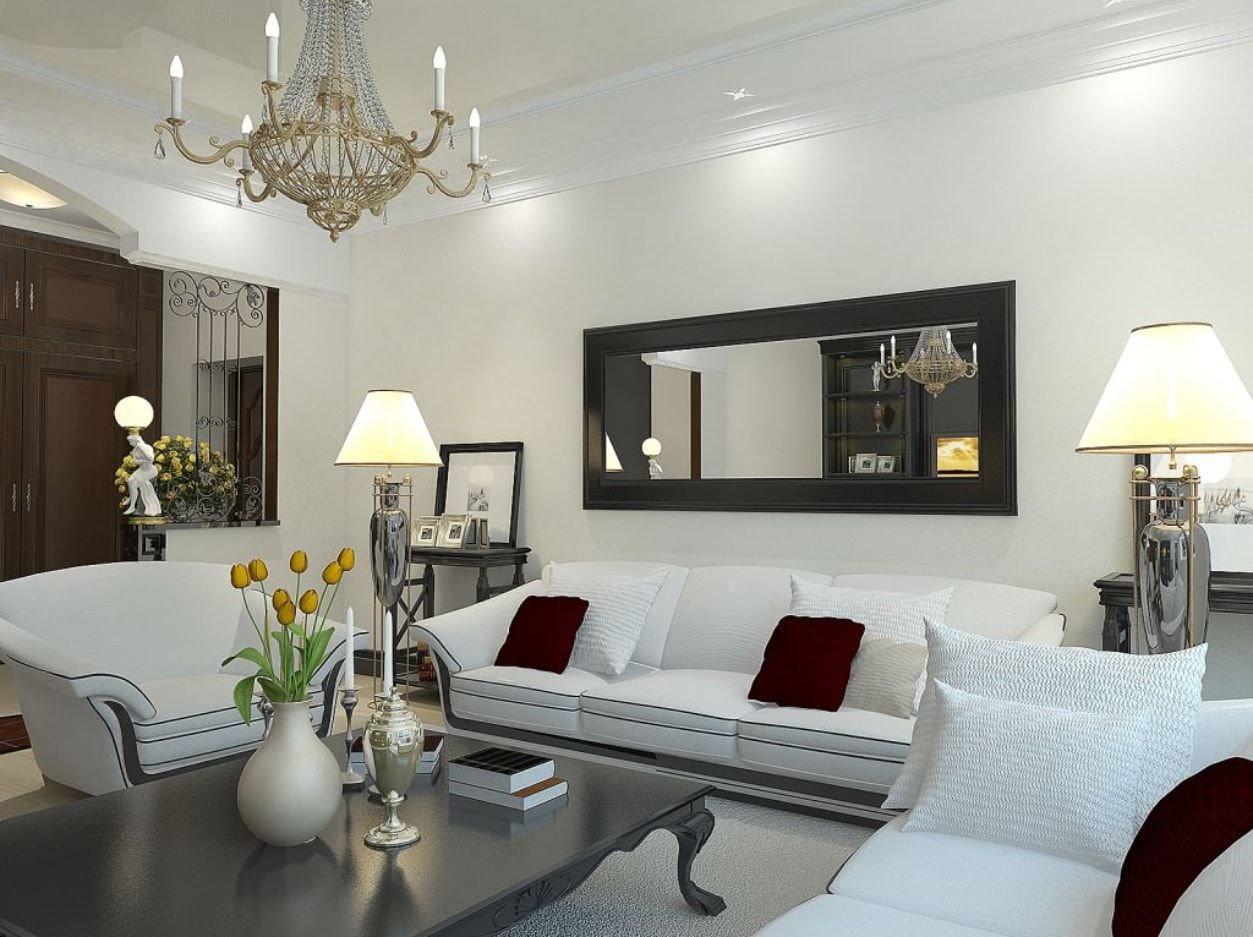 Contemporary interior of the white living room with big crystal chandelier and black framed mirror above the sofa