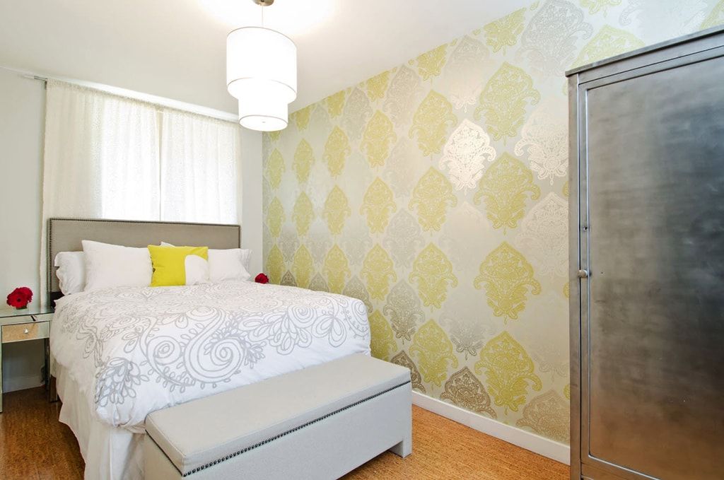 Yellow and green silkscreened wallpaper motif in the bedroom with gray ottoman