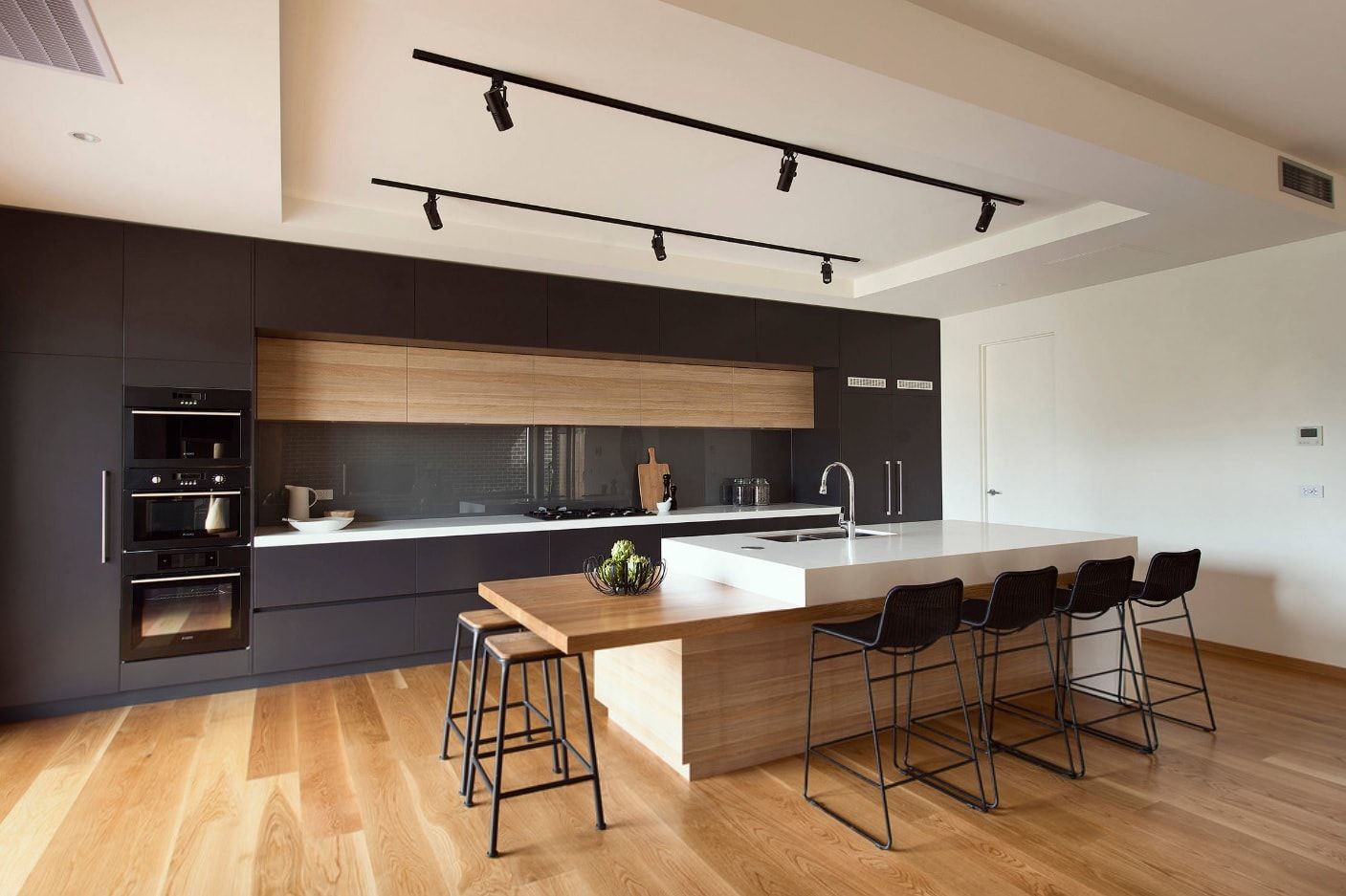 Black rods at the ceiling for lighting fixtures and wooden trimming for contrasting modern kitchen