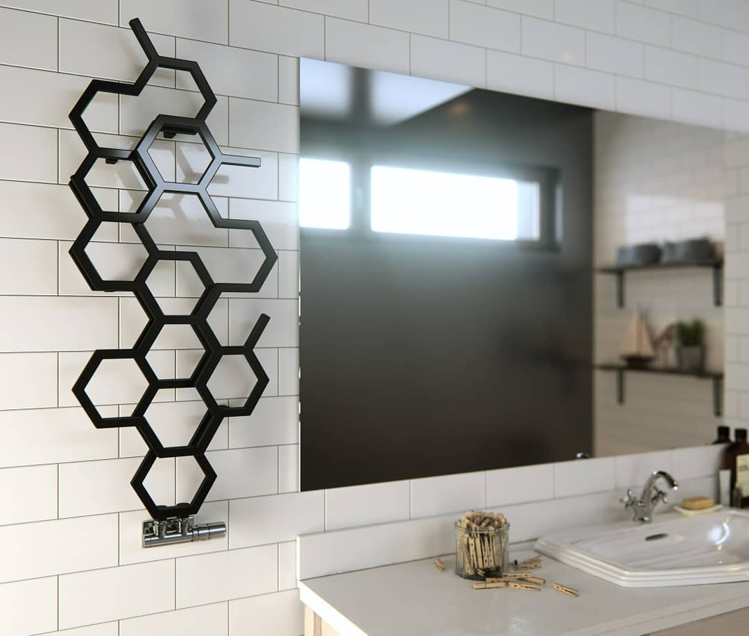 Heated Towel Rail in Bathroom Interior as Practical and Decorative Item. Unusual black honeycomb-looking towel rail for minimalistic bathroom with large mirror