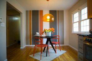 Simple but original design of the dining room with orange chairs and colorful stripes on the accent wall