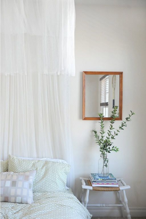 Cozy casual white bedroom with tulle and wooden framed mirror