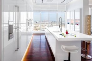 7 Home Collections by Luxury Fashion Brands. Ultramodern kitchen in the penthouse apartment with white glosy facades, backlight and dark wooden floor