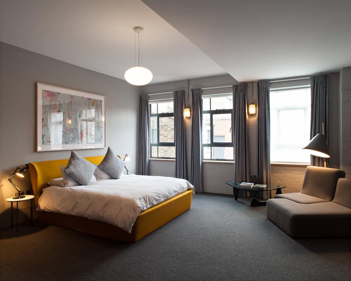 How to Breathe New Life into Your Home’s Interior Design. Great example of urban styled bedroom with brickwork wall and full of natural light despite the gray carpeting and paint