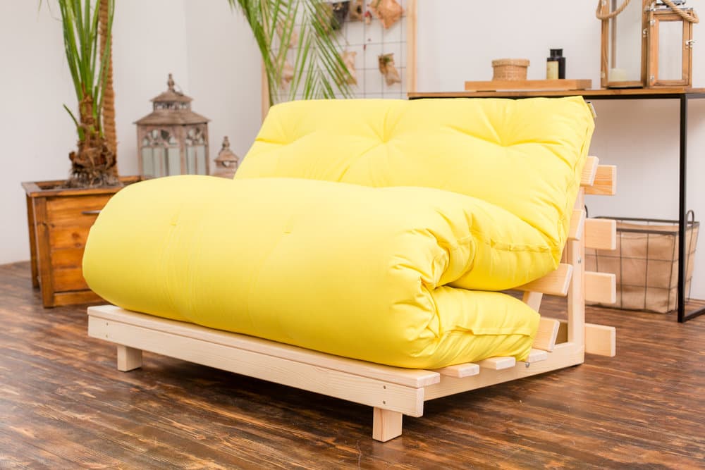 Differences Explained: The Ultimate Futon vs. Bed Comparison. Yellow minimalistic sofa on the wooden frame