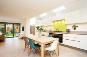 How to Make Your Kitchen Look more Expensive. Large minimalistic area with a dining zone, joyful yellow backsplash at the hob and full of light through skylights and LED fixtures