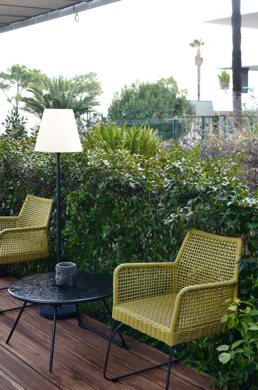 Tips to Increase the Longevity of Your Outdoor Furniture. Nice green rattan woven chairs at the wall of trimmed shrub outdoor