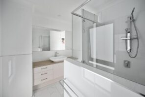 How to Fix Moisture Problems in Your Bathroom. Totally white bathroom with glass partitions and mild brown wooden vanity in modern style