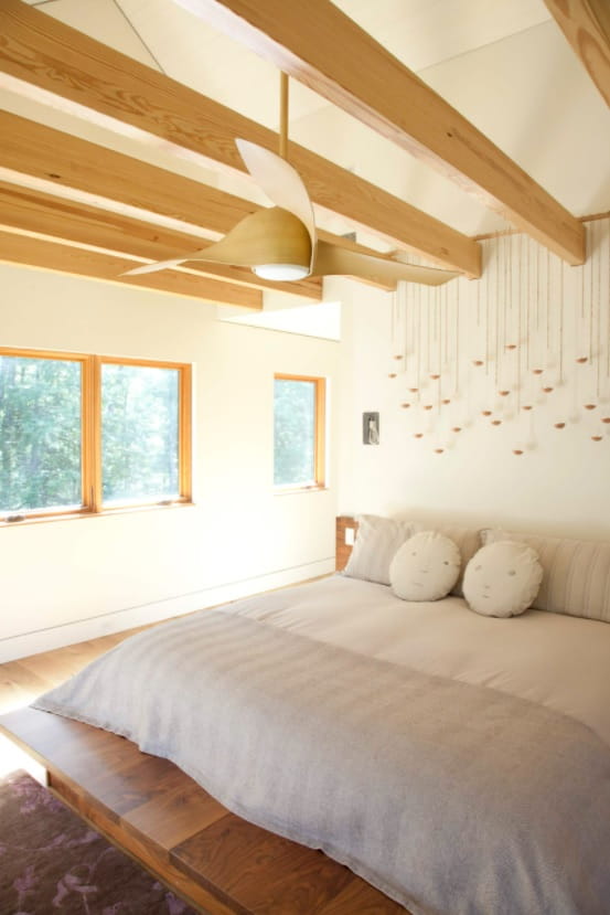 How to Choose a Stylish New Ceiling Fan. Cozy Scandinavian interior of the bedroom with wooden beams, miulti fixture lamp at the headboard and king size bed