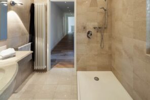 Monolithic bathroom design with sandy colored ceramic tile and white tray at the shower zone