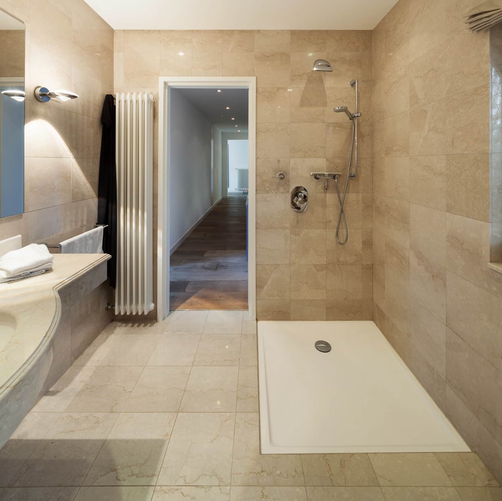 Monolithic bathroom design with sandy colored ceramic tile and white tray at the shower zone