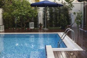 Ensure Awesome Backyard Design by Keeping Your Swimming Pool Clean. Wooden dark painteed deck and the large parasol for the backyard leisure zone