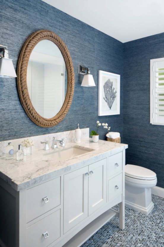 How to Make a Bathroom Much Cozier and More Stylish. Vintage mirror with gilded rim and white fruniture for the classic bathroom with embossed blue wallpaper