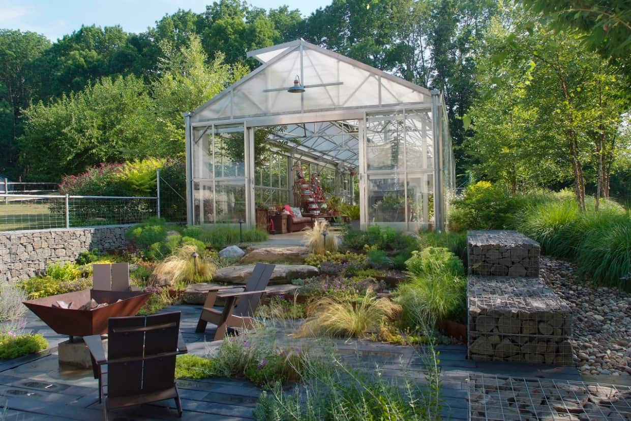 Tips On Where To Place Your Greenhouse. High structure on alluminum frame as the central piece of the backyard with stone cages as the decoration