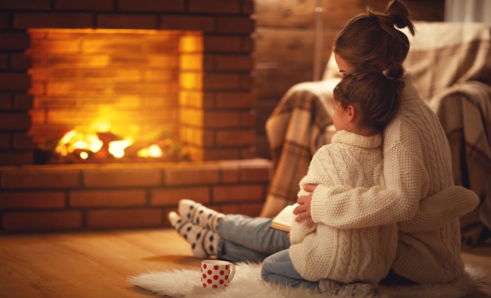 6 Ways To Get Your House Winter Ready. The woman is sitting in from on the fireplace and hugging her child